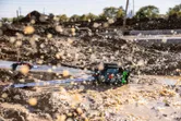 Laser-Nivelliergerät auf einer schlammigen Baustelle, wo Wasser in hellem Sonnenlicht spritzt.