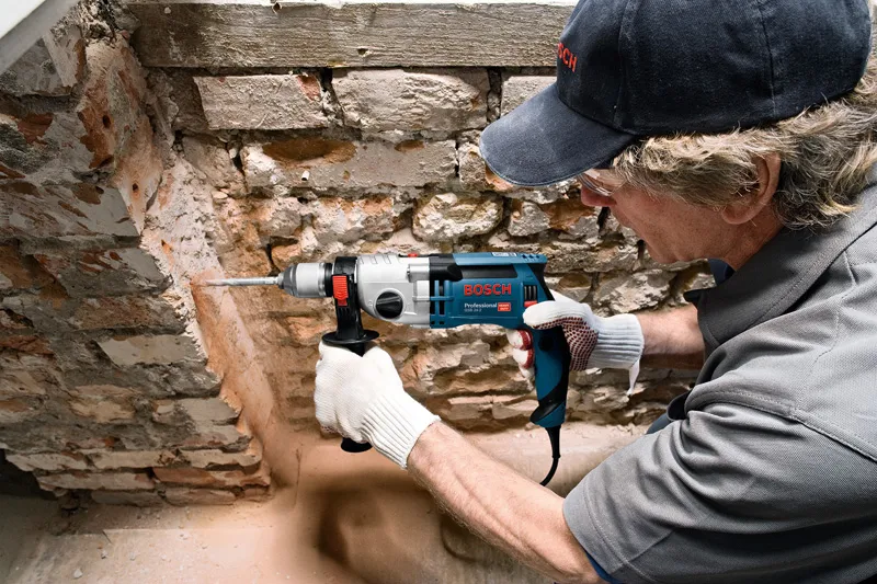Eine Person mit Sicherheitsausrüstung bohrt in eine Steinmauer.