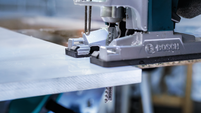 Stichsäge schneidet in einer Werkstatt eine weiße Plastikfolie durch.