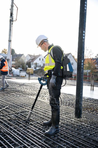 Eine Person, die Schutzausrüstung trägt, benutzt einen Betonrüttler auf einem Bewehrungsgitter.