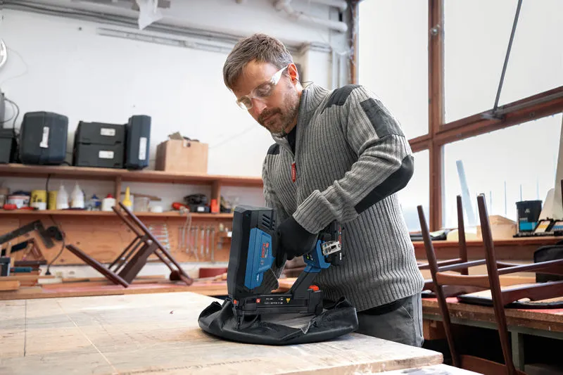 Eine Person, die Schutzausrüstung trägt, benutzt einen kabellosen Schmalrückentacker auf Stoff.