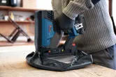 Eine Person, die Schutzausrüstung trägt, benutzt einen kabellosen Kronenhefter, um Polstermöbel zu befestigen.