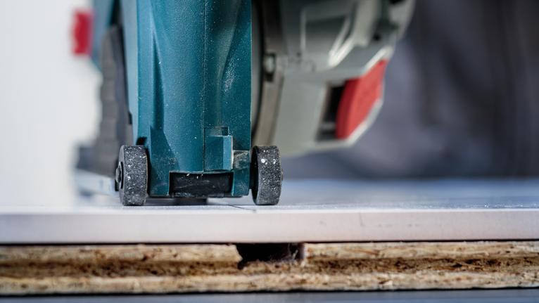 Kreissäge zum Schneiden einer auf einem Holzbrett verlegten Fliese.