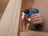 Eine Person, die Schutzausrüstung trägt, benutzt einen Akku-Bohrschrauber an einem Holzrahmen.