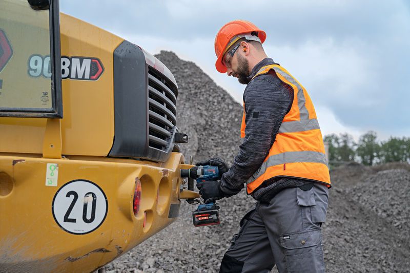 Eine Person, die Schutzausrüstung trägt, bedient an Baumaschinen einen Akku-Schlagschrauber.
