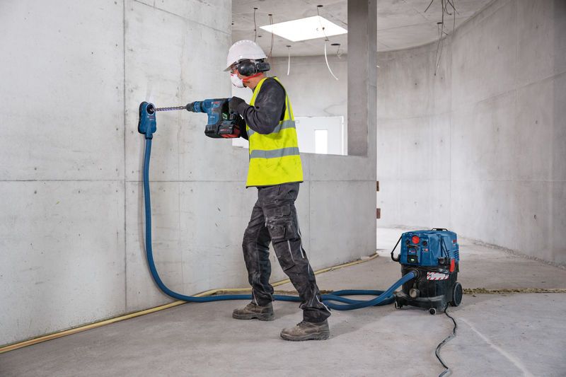 Ein Arbeiter in Schutzausrüstung bohrt mit einem akkubetriebenen Bohrhammer in Beton.
