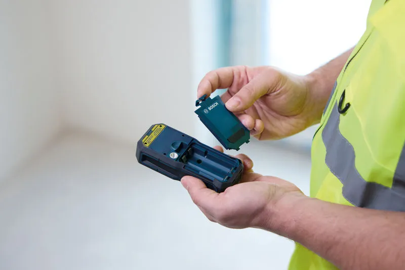 Eine Person, die Schutzausrüstung trägt, legt eine Batterie in ein Handmessgerät ein.