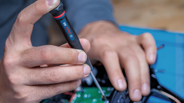 Person, die mit einem Schraubendreher elektronische Bauteile zusammenbaut.
