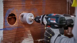 Eine Person, die Schutzausrüstung trägt, bohrt ein kreisrundes Loch in eine geflieste Wand.