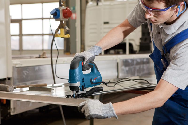 Eine Person mit Schutzausrüstung schneidet mit einer Stichsäge ein Metallblech.