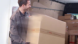 Ein Mann hebt einen großen Karton mit Bosch-Logo in einem Lieferwagen voller Pakete.