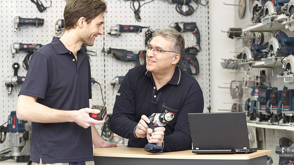 Zwei Männer stehen an einem Tisch, einer hält einen Akku-Bohrer, der andere ein Messgerät.