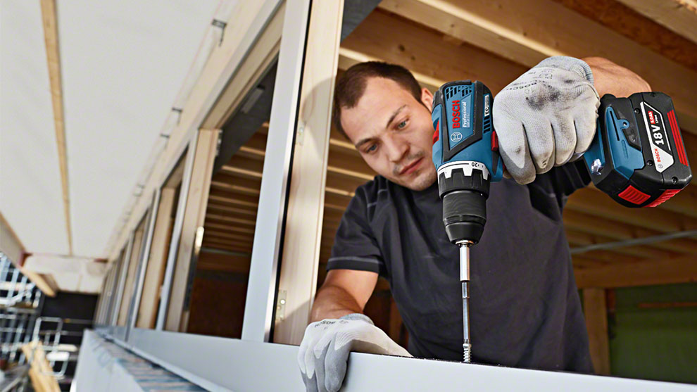 Ein Mann mit Handschuhen benutzt einen blauen Bosch Professional Akkuschrauber.