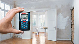 Eine Hand hält ein Bosch Professional Entfernungsmessgerät in einem renovierten Raum.