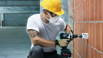 Ein Arbeiter mit gelbem Helm bohrt mit einem Bosch Professional Akku-Schrauber in eine Wand.