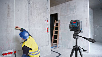 Ein Arbeiter in gelber Weste misst mit einem Laser an einer Betonwand.