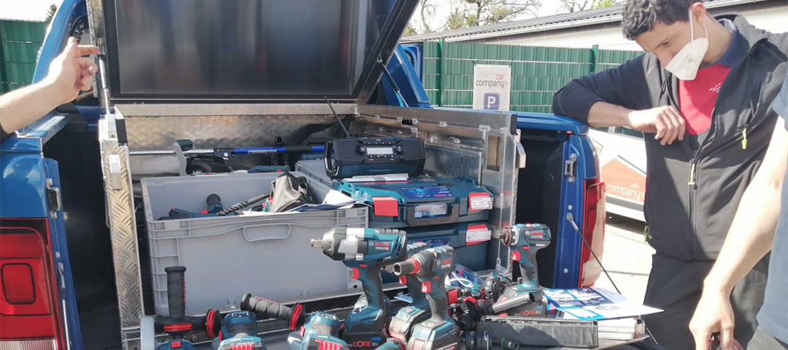 Zwei Männer betrachten Bosch Professional Werkzeuge in einem offenen Pickup-Kofferraum.