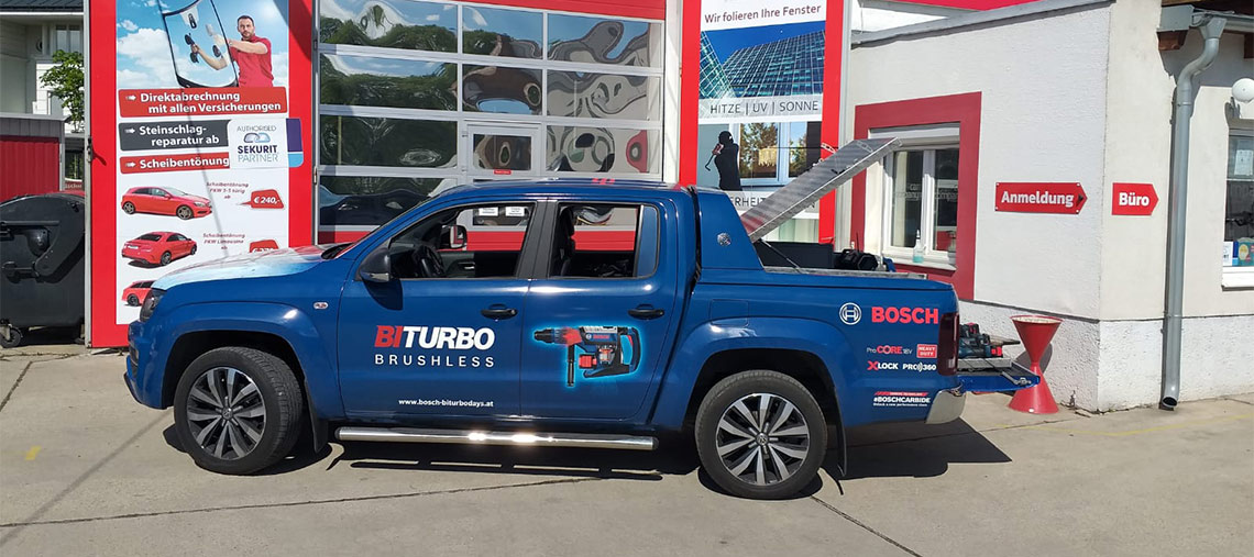 Blauer Bosch BITURBO BRUSHLESS Pickup steht an Werkstatt, Ladefläche offen, sonniger Tag.