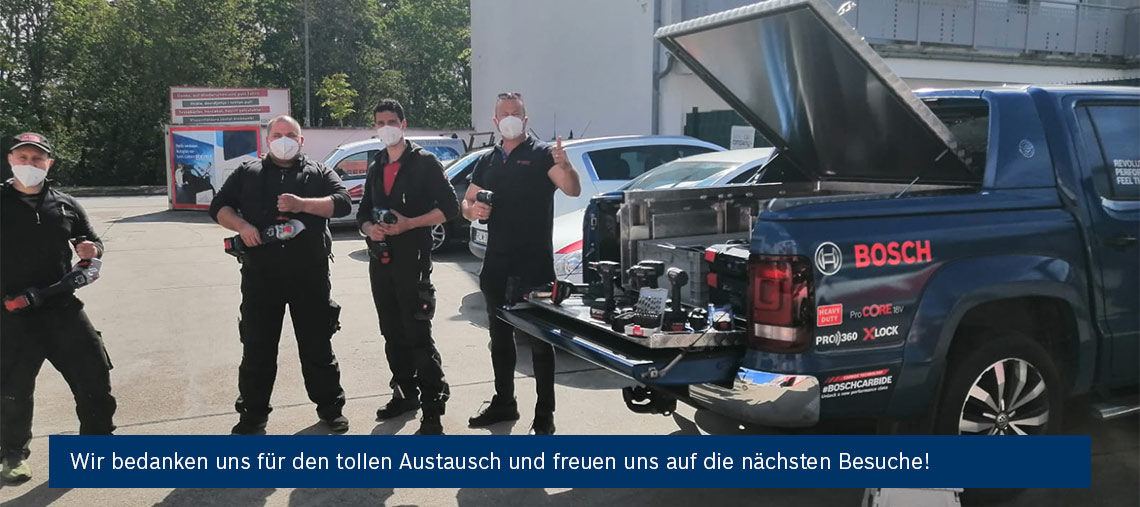 Fünf Männer in Schutzmasken halten Bosch Werkzeuge vor einem blauen Pickup im Freien.