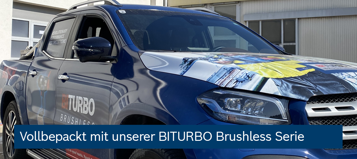 Blauer Pickup mit BITURBO Brushless Werbung, steht vor einem Gebäude.