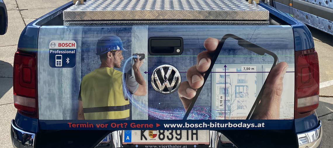 Ein blauer Pickup mit Bosch Professional Werbung, Handwerker misst mit Smartphone.