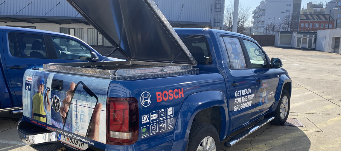 Ein blauer Bosch Professional Pickup mit offenem Ladebereich steht auf einem Parkplatz.