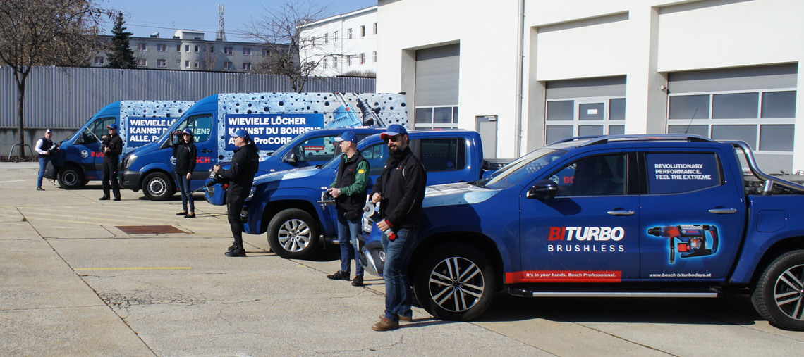 Drei Personen stehen neben blauen Bosch-Fahrzeugen auf einem Parkplatz.