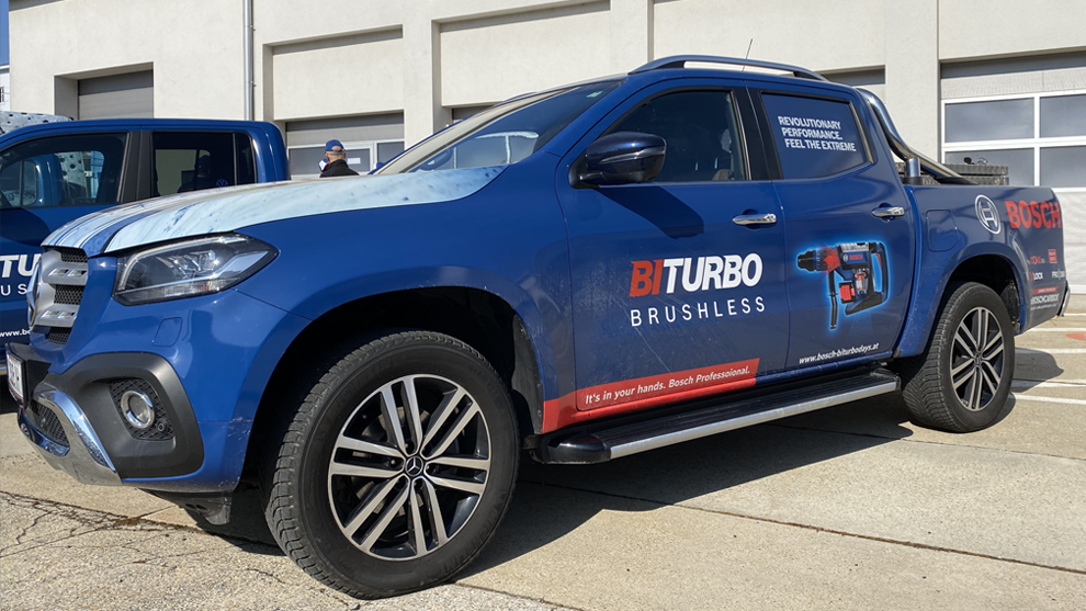 Ein blauer Bosch Professional Pickup mit BITURBO-Werbung steht vor einer Lagerhalle.