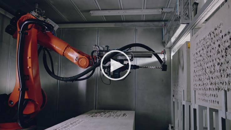 Ein orangefarbener Roboterarm bearbeitet eine graue Oberfläche in einer Werkstatt.