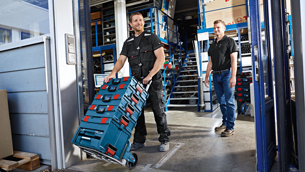 Zwei Männer in Arbeitskleidung stehen in einem Lager mit Werkzeugkisten.