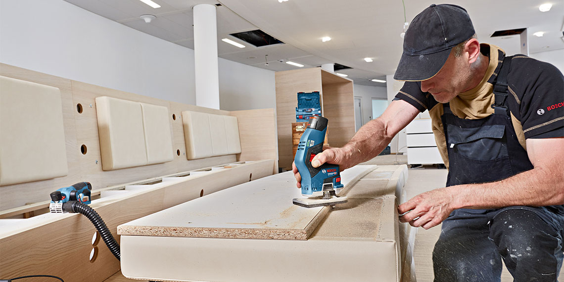 Ein Handwerker mit blauem Bosch Professional Werkzeug bearbeitet eine Holzplatte.