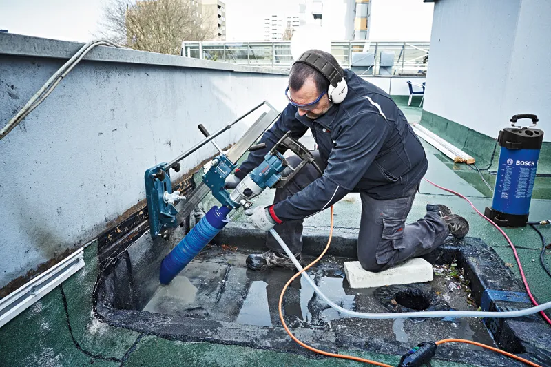 Une personne portant un équipement de sécurité perce le béton avec une foreuse diamantée montée.