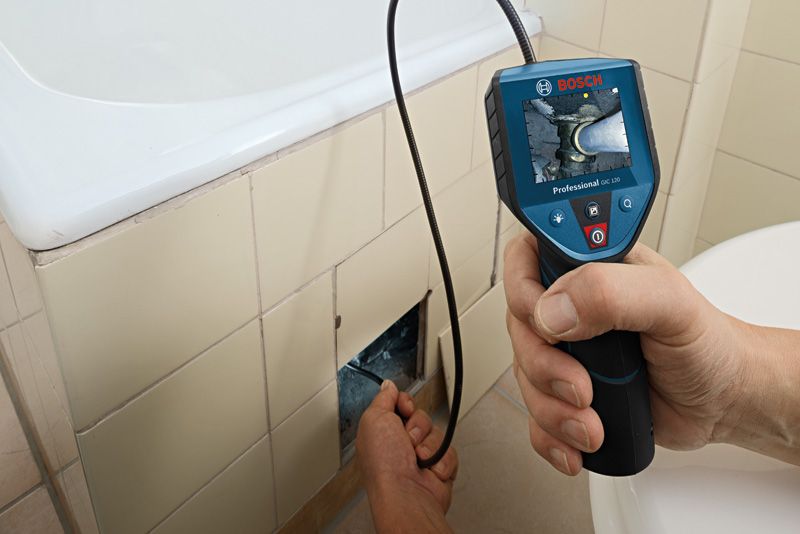 Une personne utilise une caméra d'inspection pour examiner la plomberie à l'intérieur d'un mur carrelé de salle de bain.