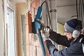 Une personne portant un équipement de sécurité utilise une rainureuse murale avec un tuyau d'extraction de poussière sur la brique.