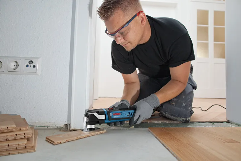 Une personne portant un équipement de sécurité coupe des lames de plancher à l'aide d'un multi-cutter près d'une porte.