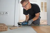 Une personne portant un équipement de sécurité coupe des lames de plancher à l'aide d'un multi-cutter près d'une porte.