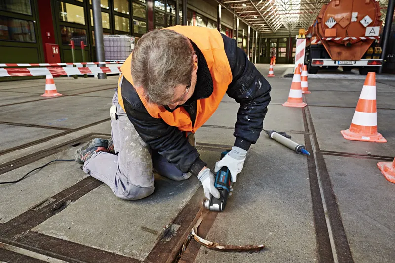 Une personne portant un équipement de sécurité utilise un multi-coupe pour retirer du matériau d'un joint de béton.