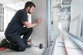 Sur un chantier de construction, une personne trace des lignes sur une cloison sèche à l'aide d'un niveau laser.