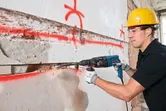 Une personne portant un équipement de sécurité utilise un marteau perforateur pour creuser une rainure dans un mur en béton.
