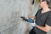 Une personne portant un équipement de sécurité perce un mur en béton avec un marteau perforateur.