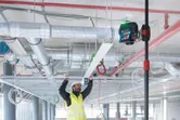 Une personne portant un équipement de sécurité aligne un cadre de plafond à l'aide d'un outil de nivellement laser.
