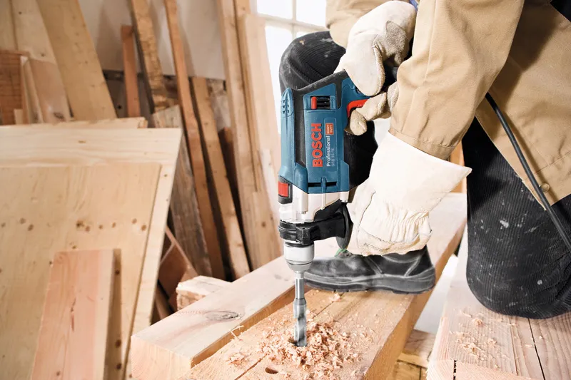 Une personne portant un équipement de sécurité perce une planche de bois dans un atelier.