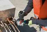 Une personne portant un équipement de sécurité coupe des barres d’armature dans du béton avec une meuleuse d’angle sans fil.