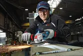 Une personne portant un équipement de sécurité meule du métal avec une meuleuse d'angle, ce qui provoque des étincelles.