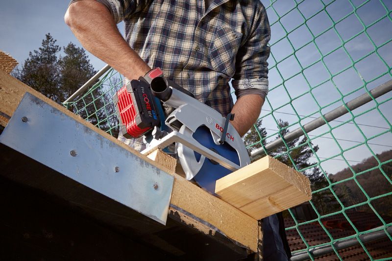 Une personne coupe une poutre en bois avec une scie circulaire sur un chantier de construction.