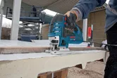 Une personne portant un équipement de sécurité utilise une scie sauteuse pour couper un panneau à l'extérieur.