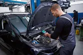 Une personne portant un équipement de sécurité inspecte le moteur d'une voiture avec une caméra thermique.
