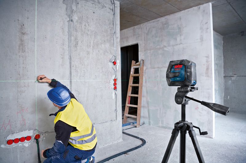 Une personne portant un équipement de sécurité marque un mur à l'aide d'un niveau laser.