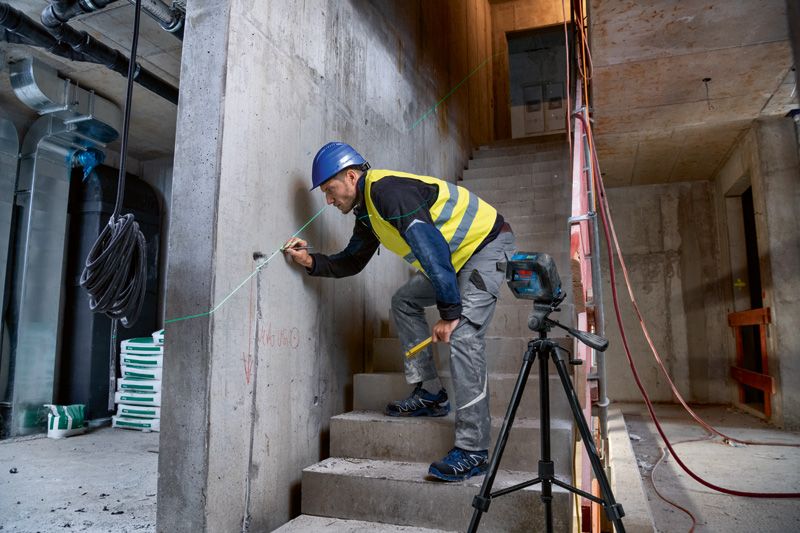 Une personne portant un équipement de sécurité marque un mur en béton à l'aide d'un niveleur laser.
