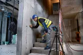 Une personne portant un équipement de sécurité marque un mur en béton à l'aide d'un niveleur laser.